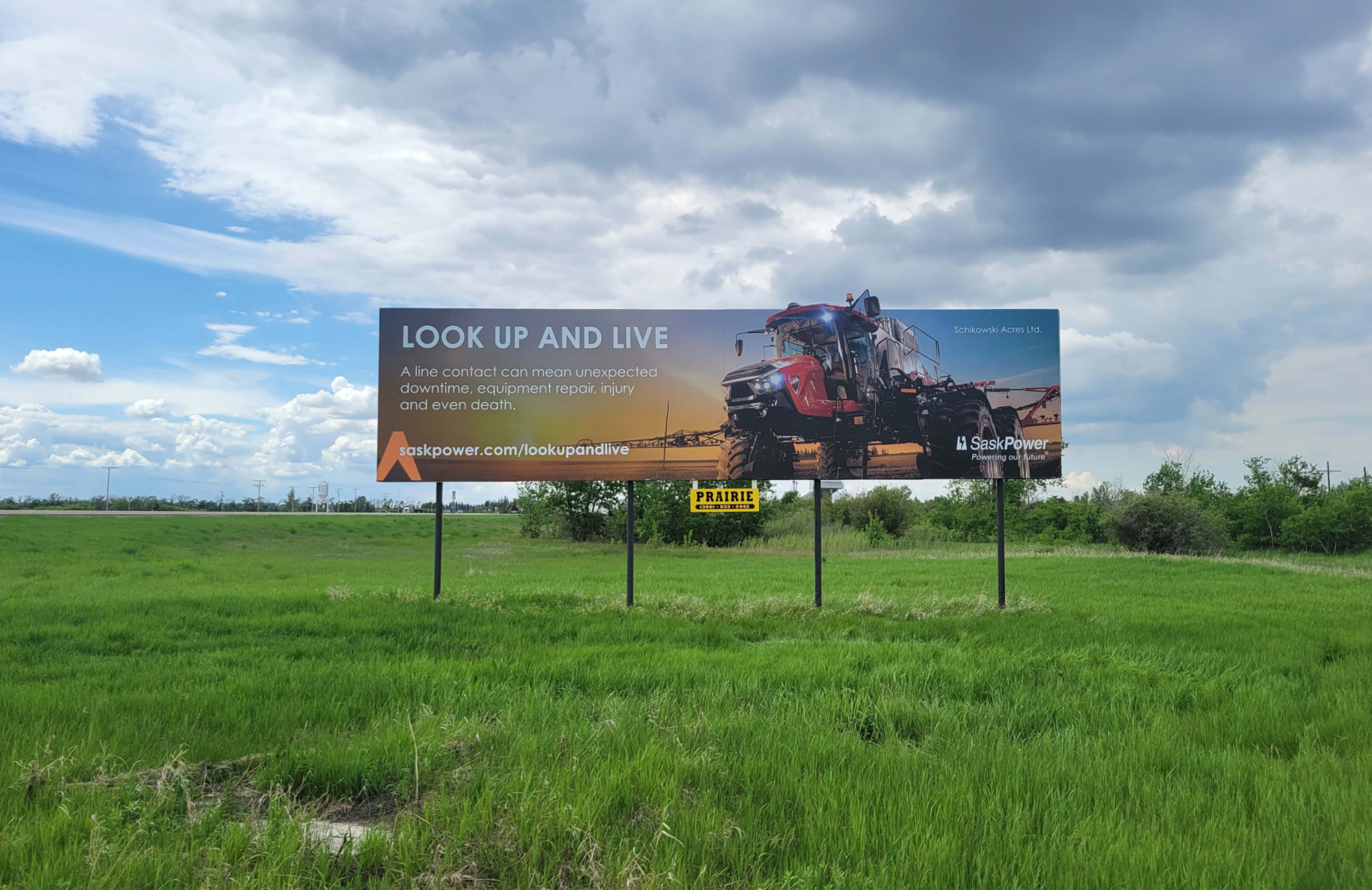 A photo of the SaskPower billboard in real life, in a green field with a blue sky background